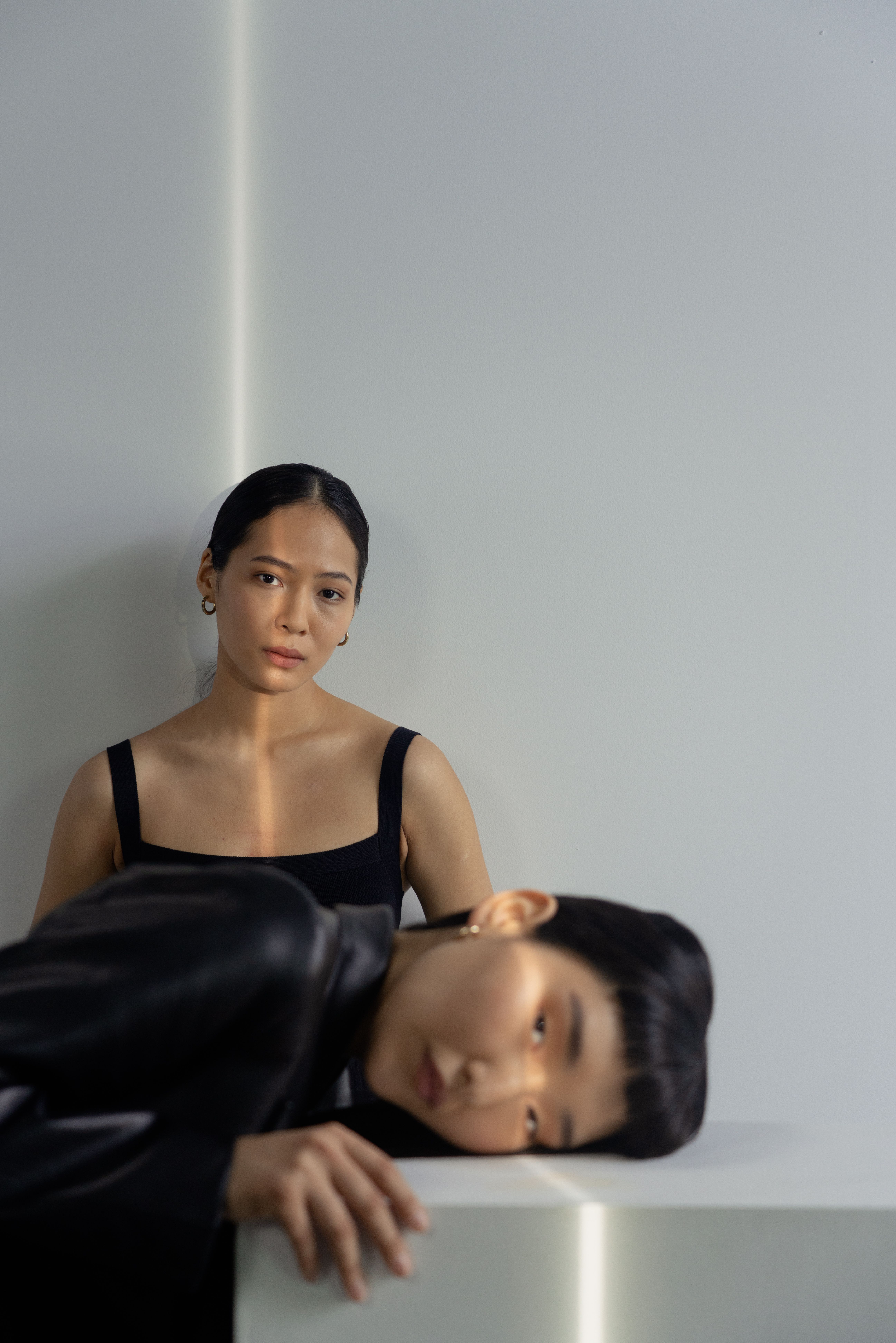 Two Asian women in black attire posing artistically indoors, showcasing modern fashion and style.