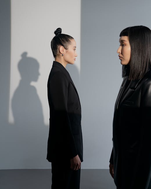 Two women in stylish black outfits stand face-to-face in a well-lit studio, casting unique shadows.