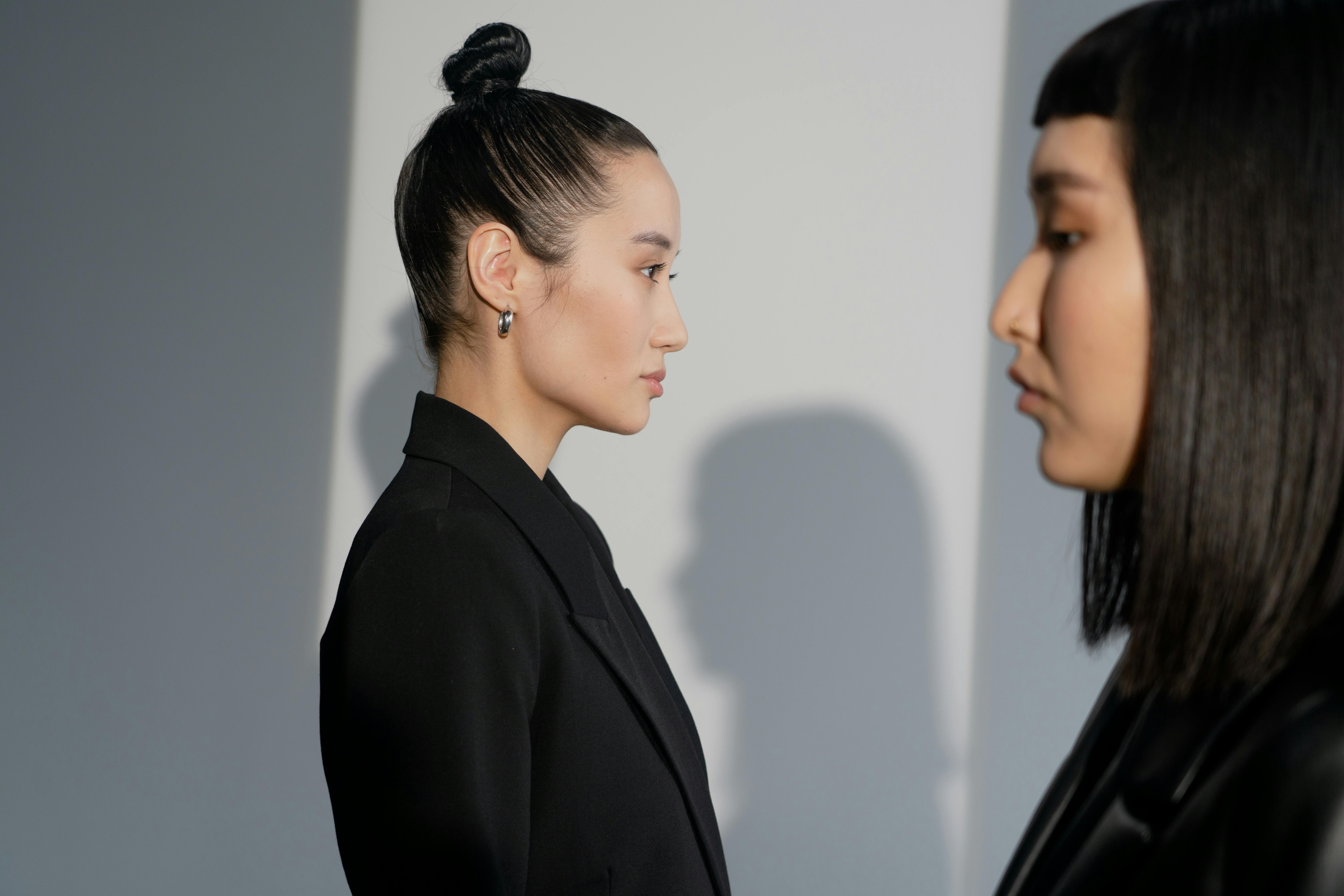 Side profile of two women in formal attire, highlighted by soft lighting and a minimalist background.