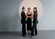 三位身着黑色时装的女性在极简主义背景下的时尚肖像