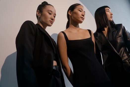 Three stylish women posing in chic black outfits against a minimalist backdrop.