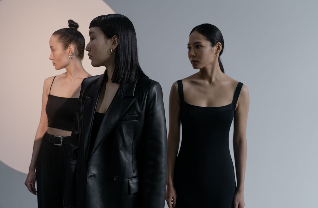 three women in stylish black outfits pose elegantly against a studio b