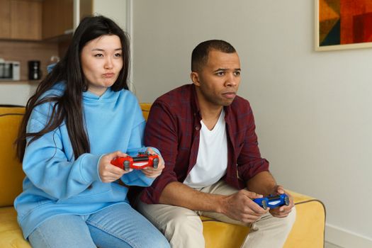 Interracial couple enjoying video games together on a cozy sofa in the living room.