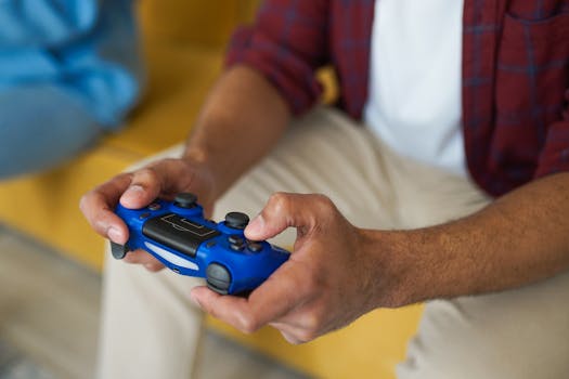 Hands holding a blue wireless game controller on a comfortable sofa indoors.