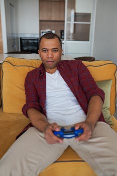 A man sitting on a sofa, intensely focused while playing video games indoors.