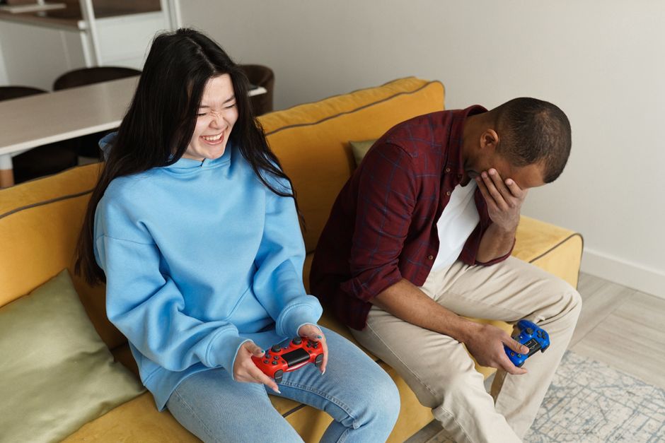 Smiling interracial couple playing video games on a cozy sofa indoors, sharing a fun moment together.