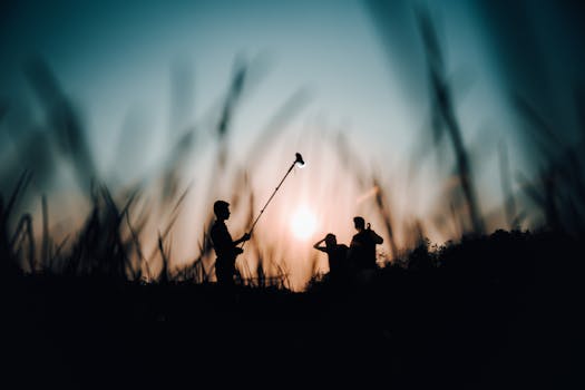 Captivating silhouettes of people with a boom mic at sunset, set against a grass field backdrop.