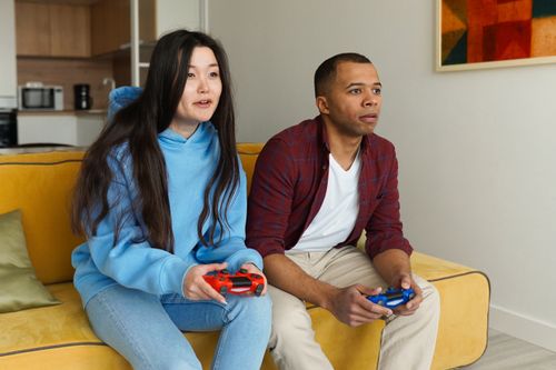 Free A happy interracial couple playing video games on a sofa, with wireless controllers indoors. Stock Photo