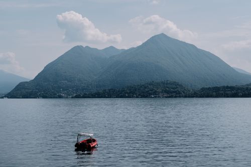 Free A serene view of a red boat on a calm mountain lake, surrounded by lush green hills. Stock Photo