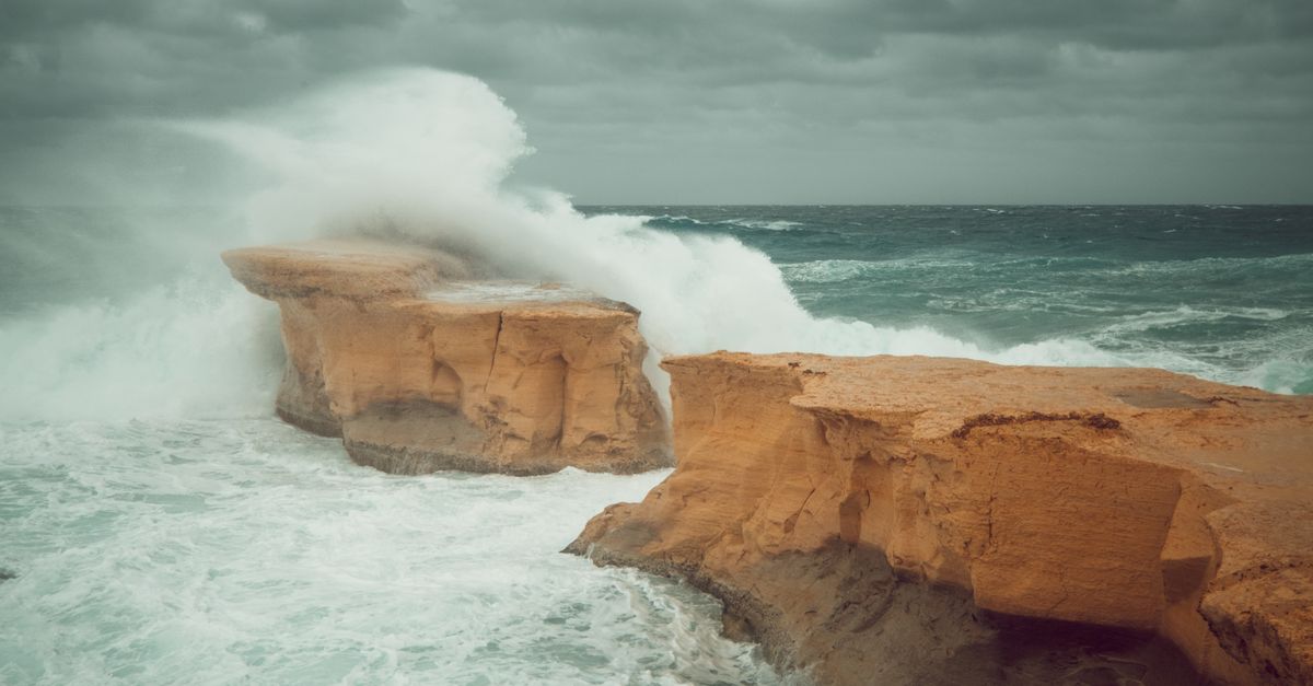 Powerful waves crash against limestone cliffs in Gozo, Malta, creating a dramatic seascape.