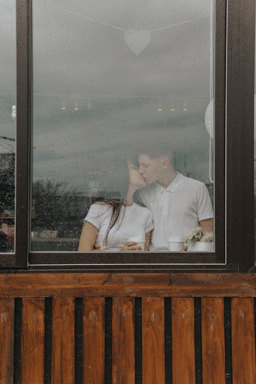 Romantic couple with takeaway coffee kissing behind window in cafe