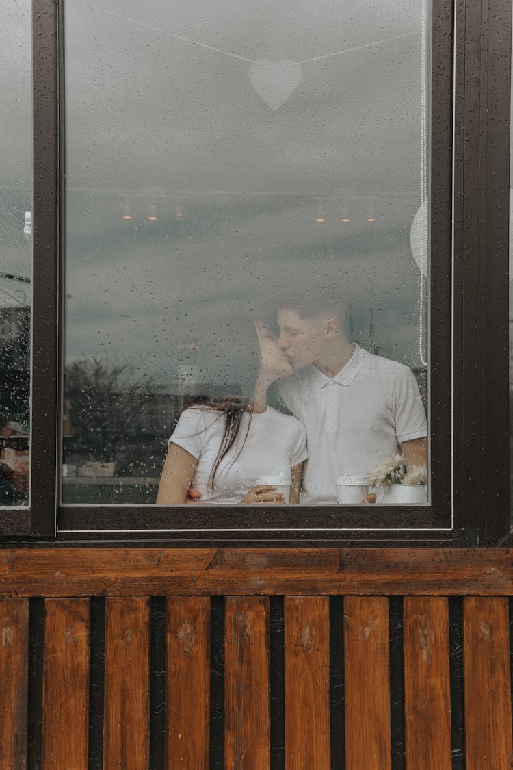 Romantic Couple With Takeaway Coffee Kissing Behind Window In Cafe