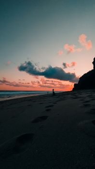 A peaceful sunset over a tranquil beach with silhouetted figure and vibrant clouds.