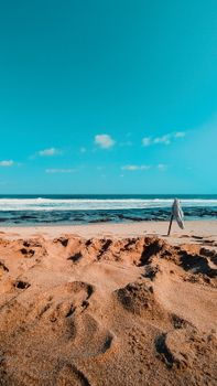 A calm beach scene with ocean waves, sandy shores, and a flag under a clear blue sky.