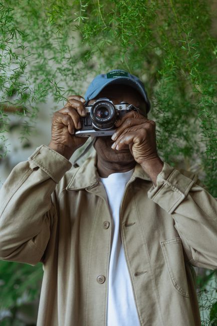 An adult holding a vintage camera amidst lush green foliage, capturing moments with passion.