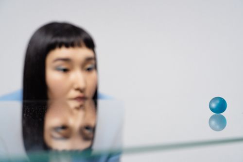 Free A woman gazes thoughtfully at a blue ball with reflections on a glass surface. Stock Photo