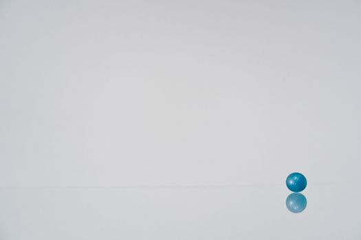 A solitary blue ball resting on a reflective white surface in a minimalist setting.