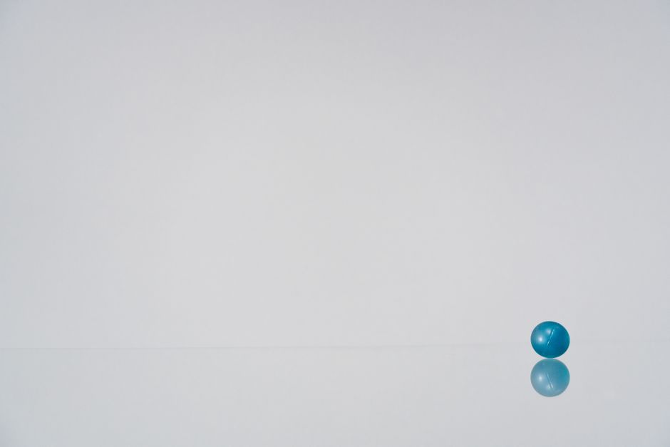 A solitary blue ball resting on a reflective white surface in a minimalist setting.