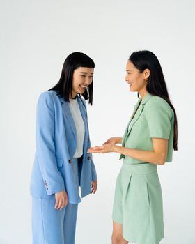 Two stylish women in pastel suits sharing a happy moment against a white studio background.