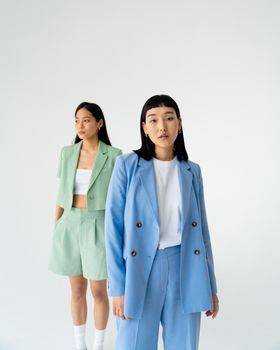 Two Asian women posing in pastel suits during a stylish studio fashion shoot on a white background.