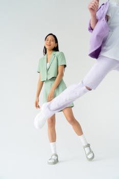 A stylish Asian woman in pastel outfit poses with a playful vibe in a studio setting.