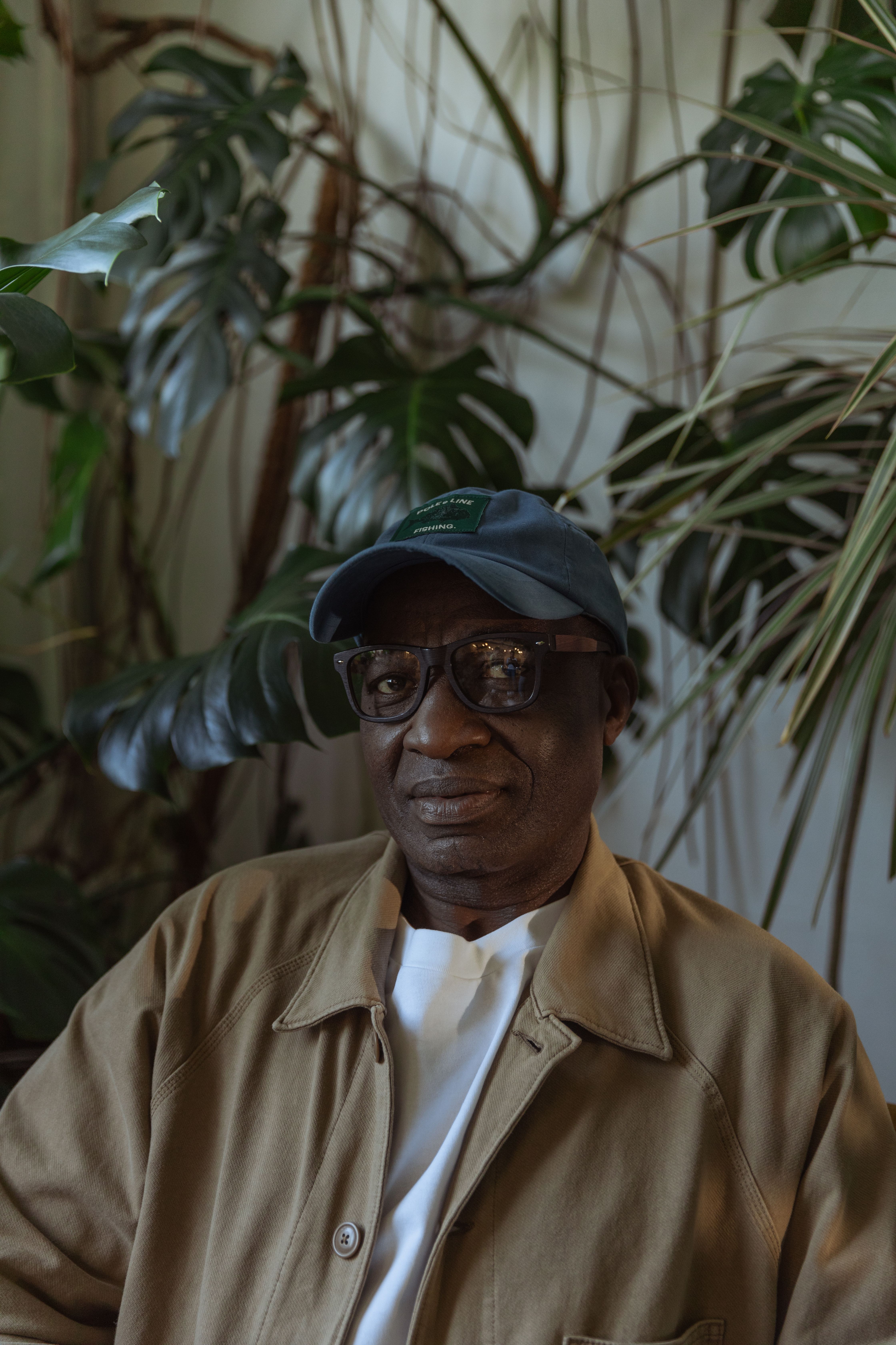 Portrait of a senior man wearing a baseball cap surrounded by lush indoor plants.