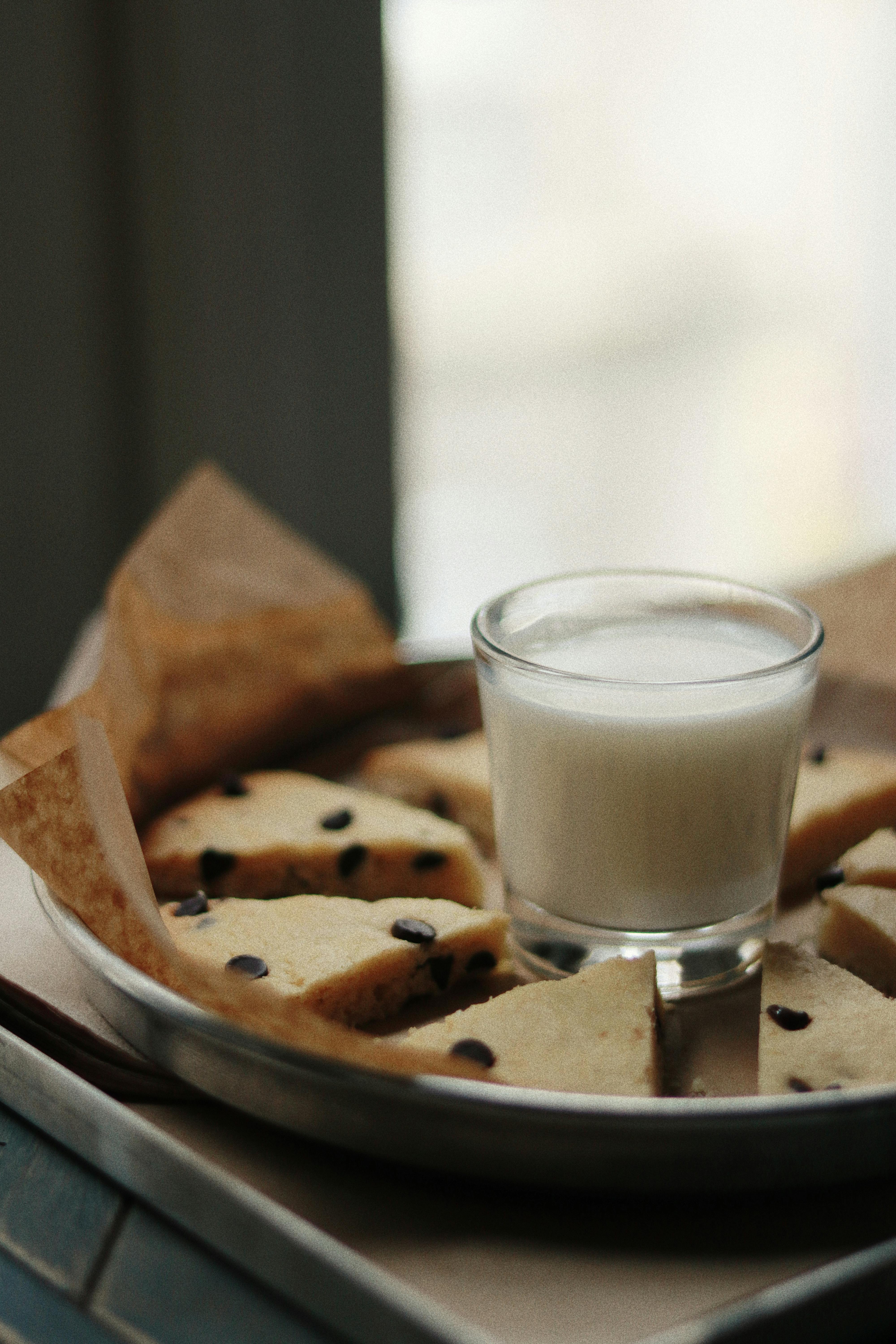 Glass of milk among tasty pie pieces with chocolate chips on parchment paper in baking pan at home