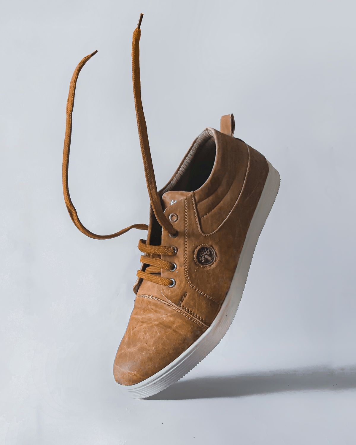 A brown suede shoe floating with its laces undone