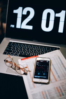 Laptop, smartphone, and financial document on a desk with clock display.