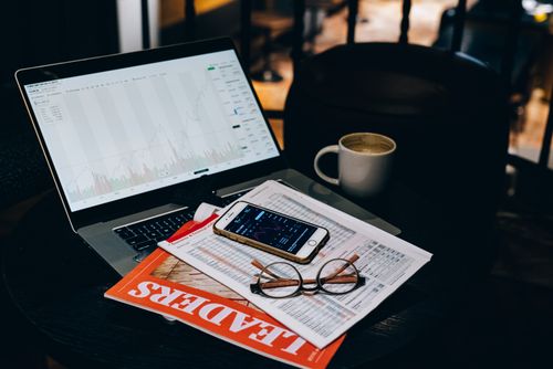 Free A cozy office desk setup with a laptop displaying stock charts, coffee, and documents. Stock Photo