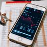 A smartphone displays a red, downward-trending stock market chart resting on financial documents.