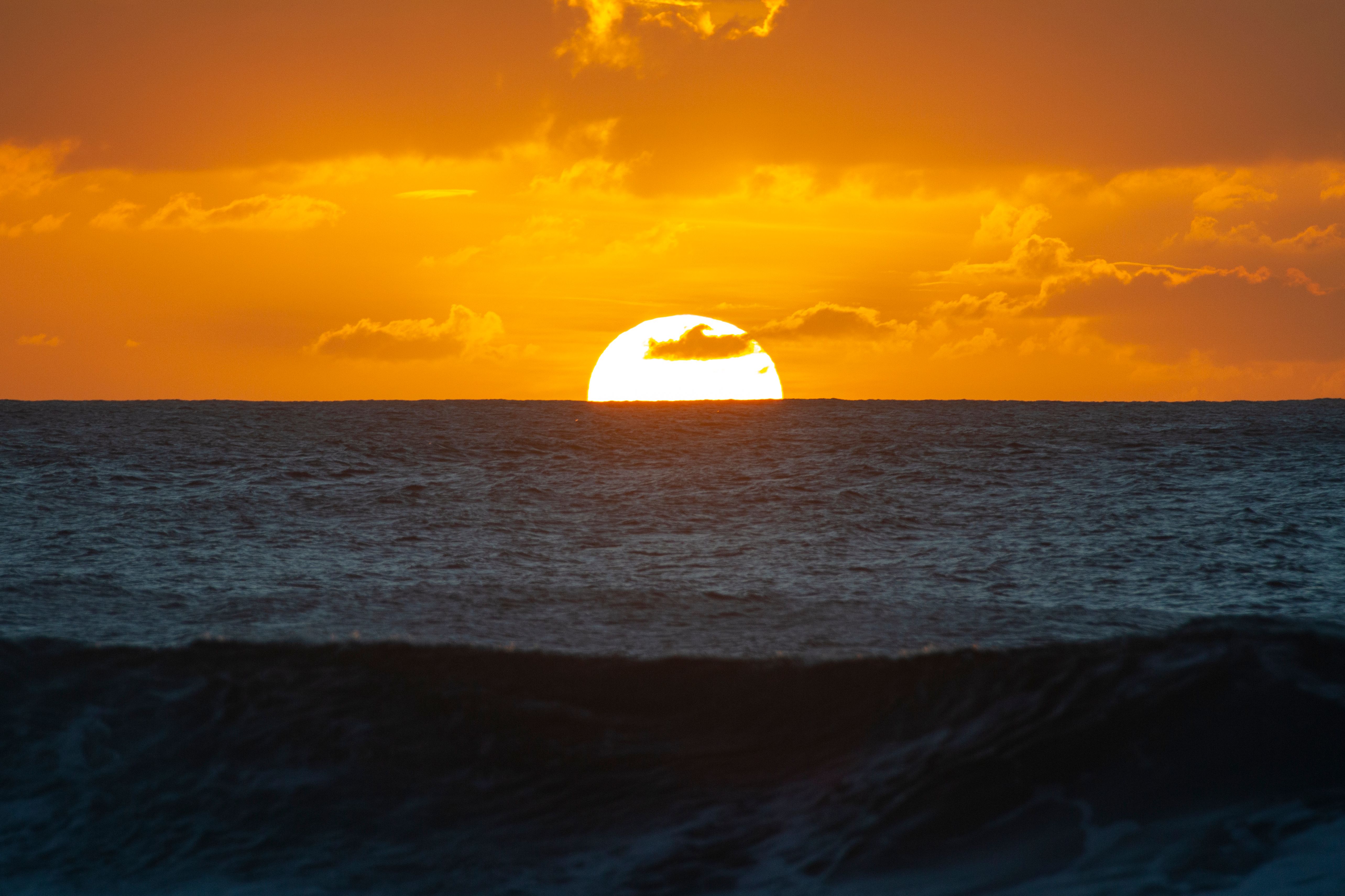 A sunset over the ocean with a bright orange sky · Free Stock Photo