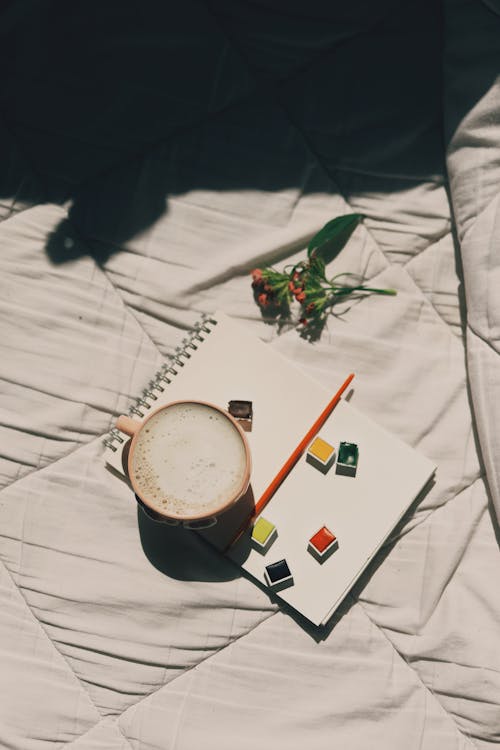 Free From above of ceramic cup of latte placed on notepad in comfortable bed in sunny day Stock Photo