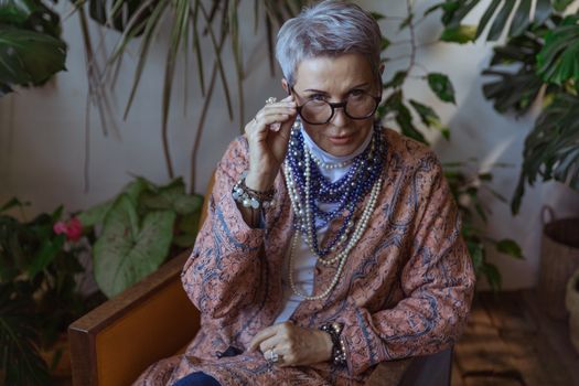 Elegant senior woman in boho style, posed indoors with a vibrant fashion touch.