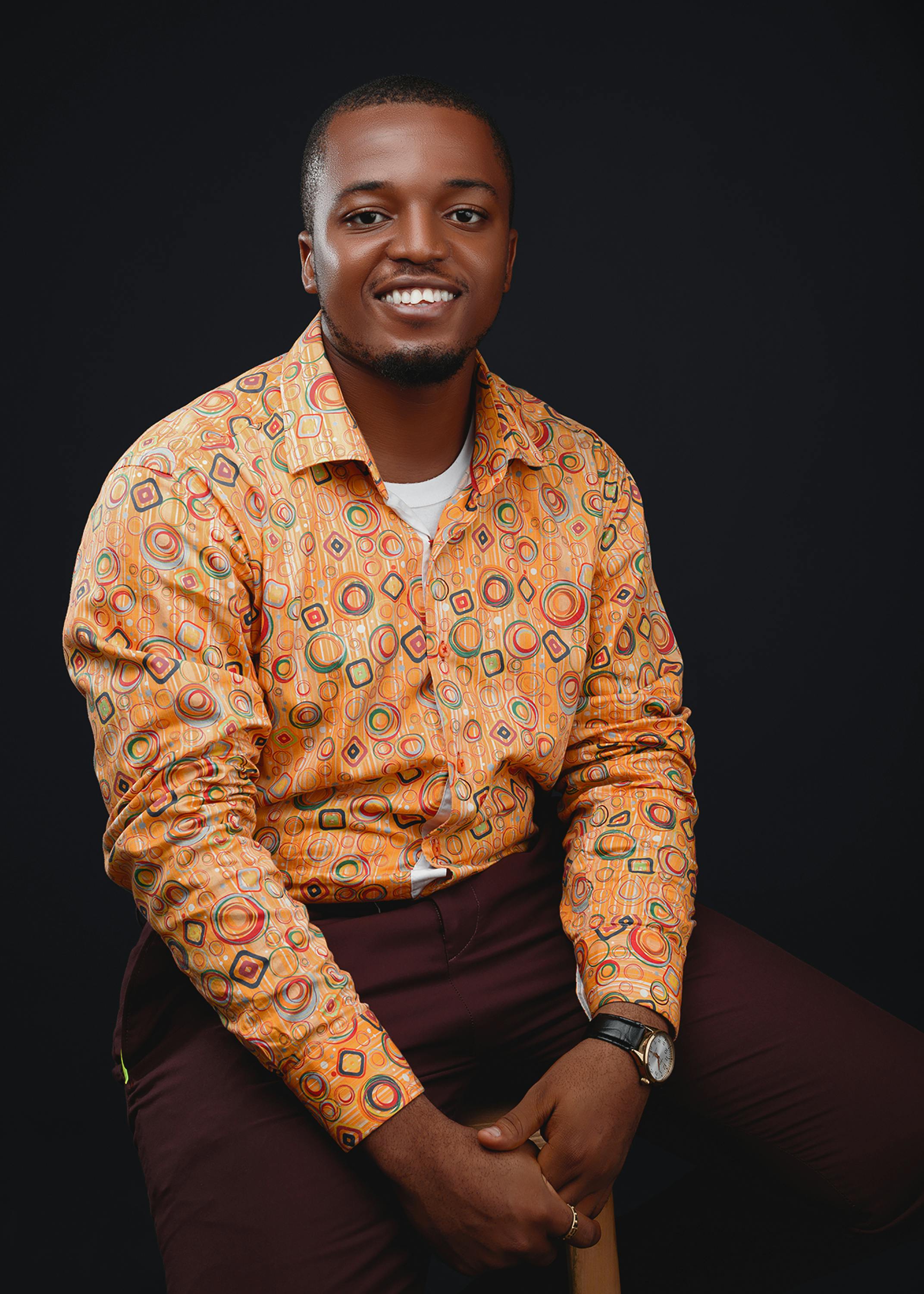 Cheerful African man in a vibrant patterned shirt posing against a dark backdrop.