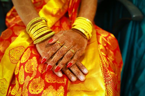 Free Close-up of hands adorned with henna, gold bangles and rings, on vibrant traditional Indian attire. Stock Photo