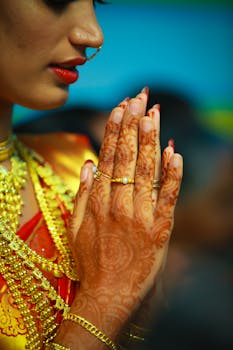 Close-up of an Indian bride with henna designs, adorned in gold jewelry, praying.