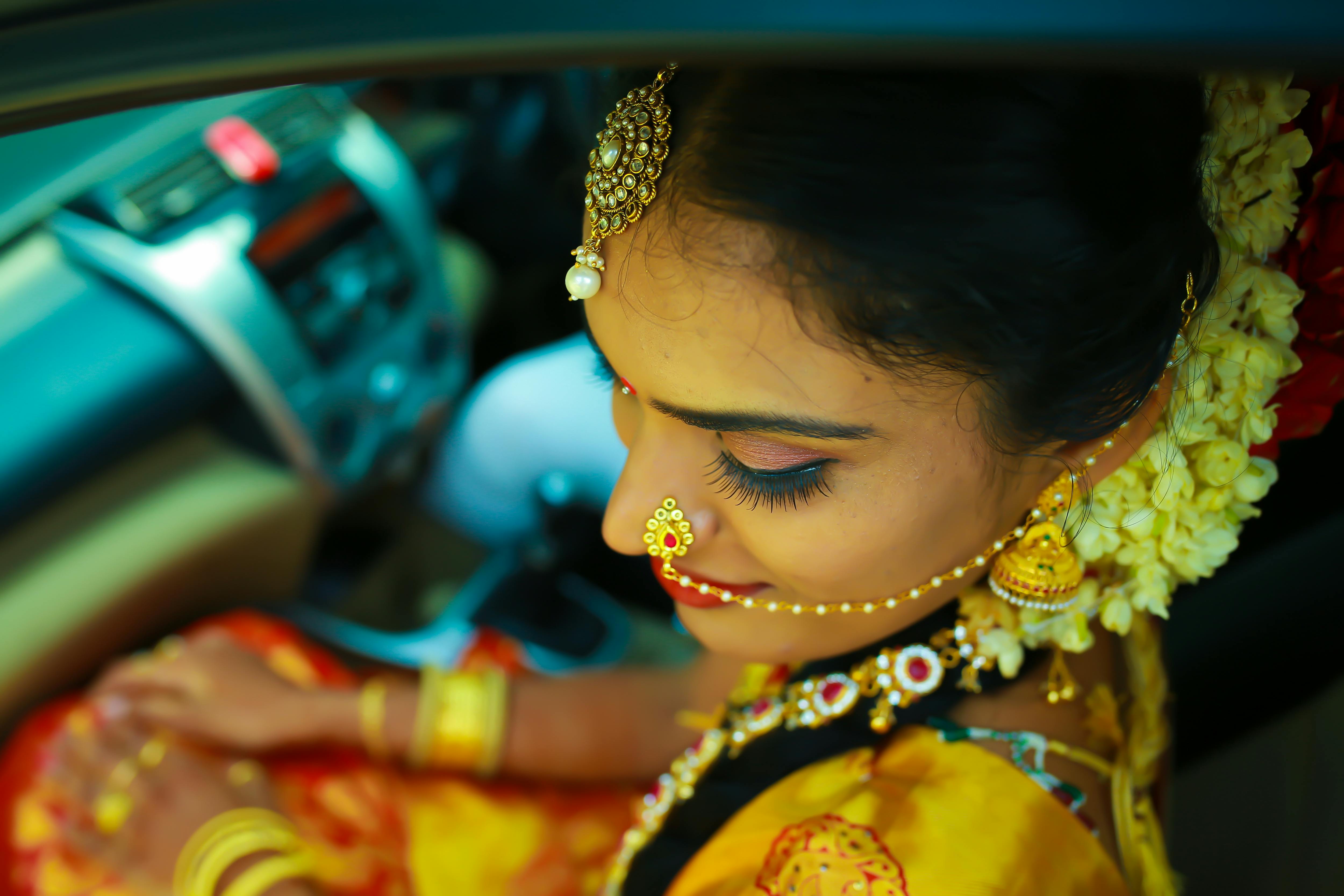 Close-up of an Indian bride adorned with traditional jewelry and flowers, captured from above in vibrant colors.