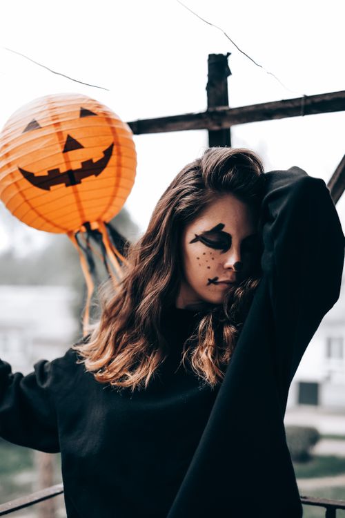 Free Stylish portrait of a young woman in Halloween makeup, posing with a pumpkin lantern outdoors. Stock Photo