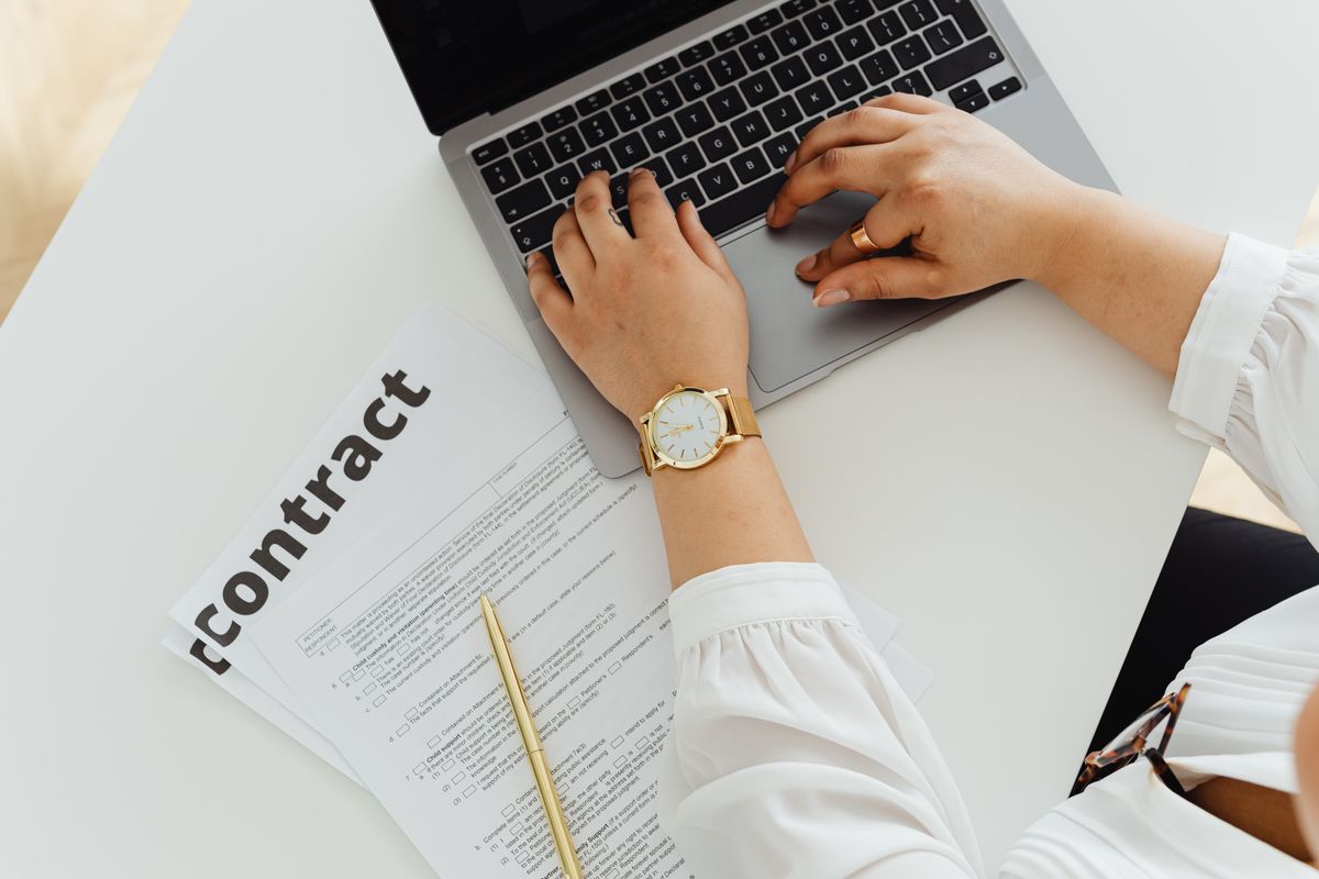 Responsable d'organisme de formation travaillant sur son ordinateur à côté d'un contrat papier, transition du papier vers le numérique