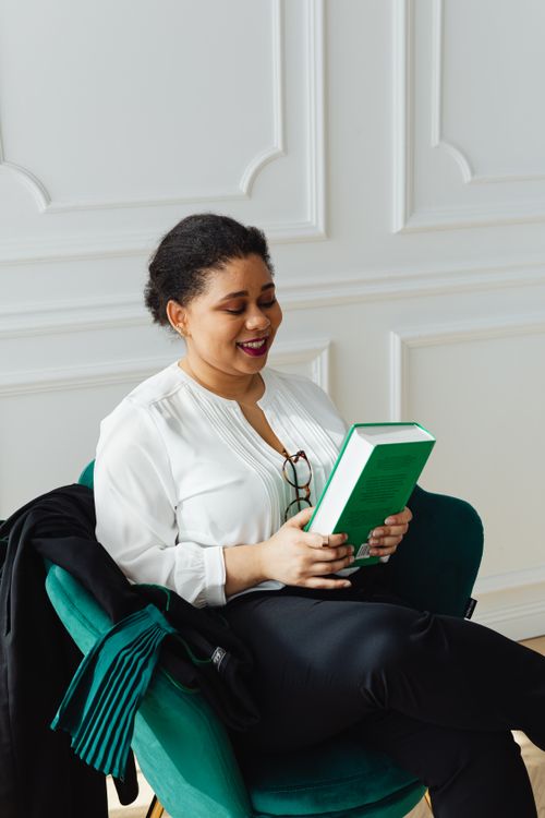 Free Elegant woman in an armchair enjoying a good book in a bright indoor setting. Stock Photo