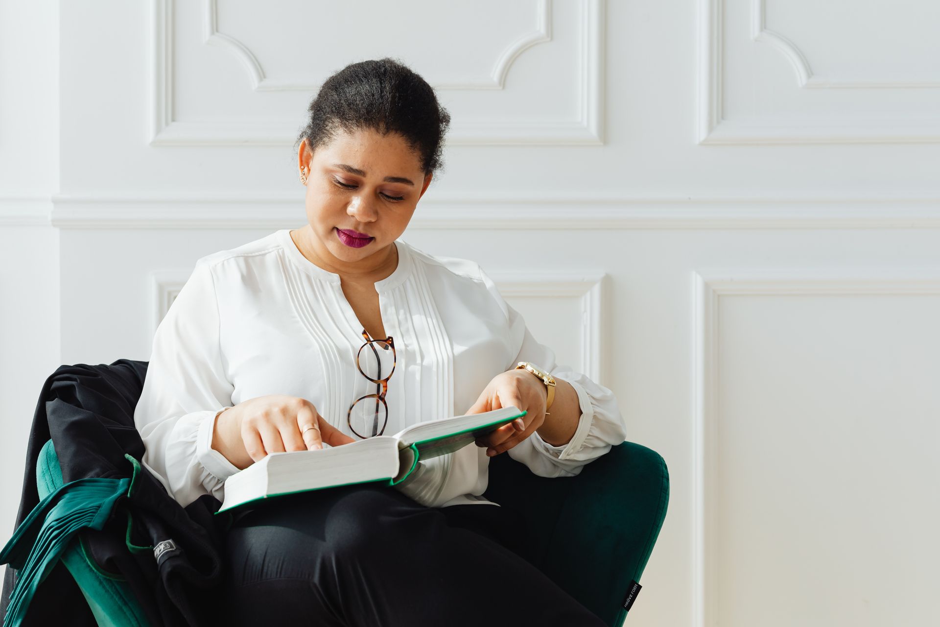 A woman sitting in a stylish office reading a book, offering a professional and serene atmosphere.