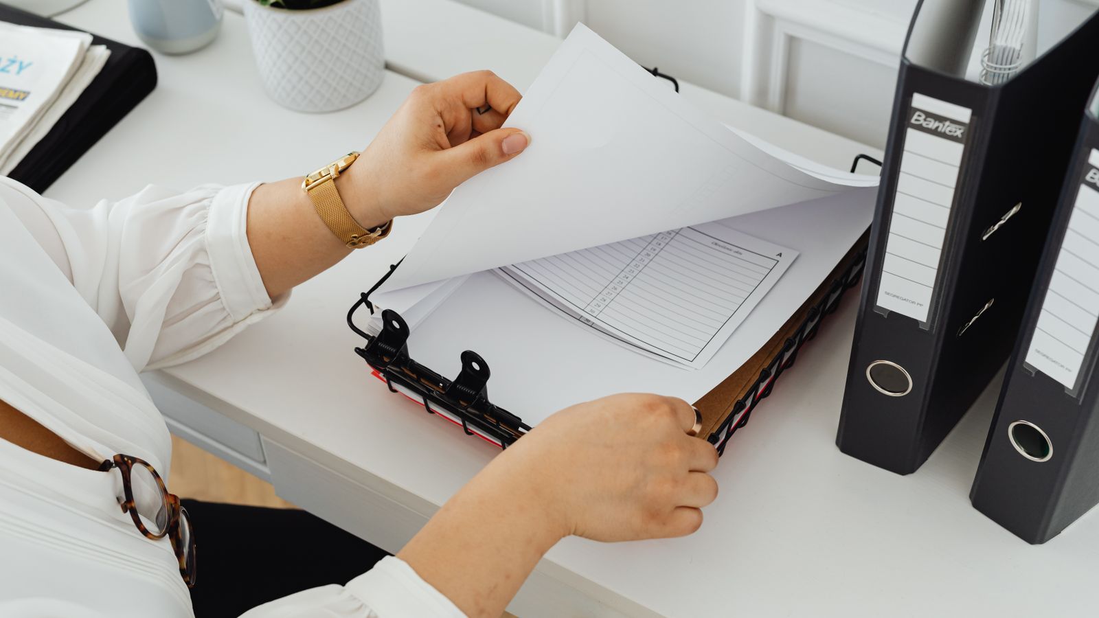 Hands sorting through papers in a binder on a desk