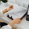A business professional's hands turning the pages of a freshly printed document in an open binder on a white desk.