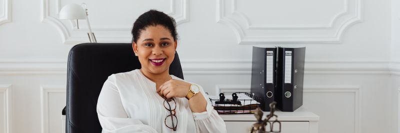Confident woman in a professional office setting with legal books and statue, exuding a sense of authority.