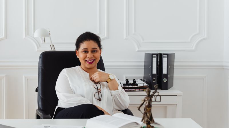 Confident woman in a professional office setting with legal books and statue, exuding a sense of authority.