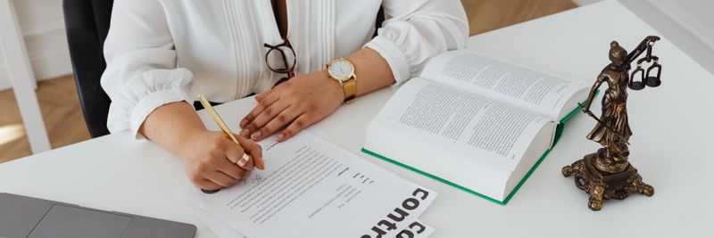 Woman in office writing on contracts, with law books and laptop on table.
