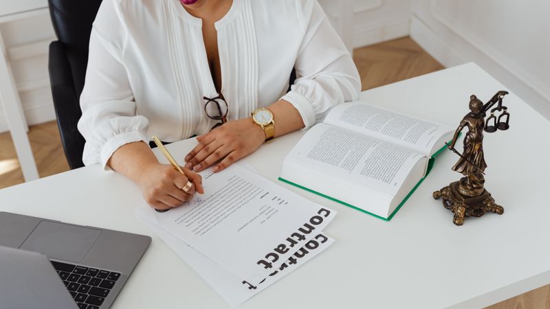 Woman in office writing on contracts, with law books and laptop on table.
