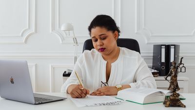 Abogada escribiendo en su escritorio junto a un laptop, un libro y una figura de la justicia