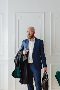 Confident businessman with beard and glasses, holding a briefcase indoors.